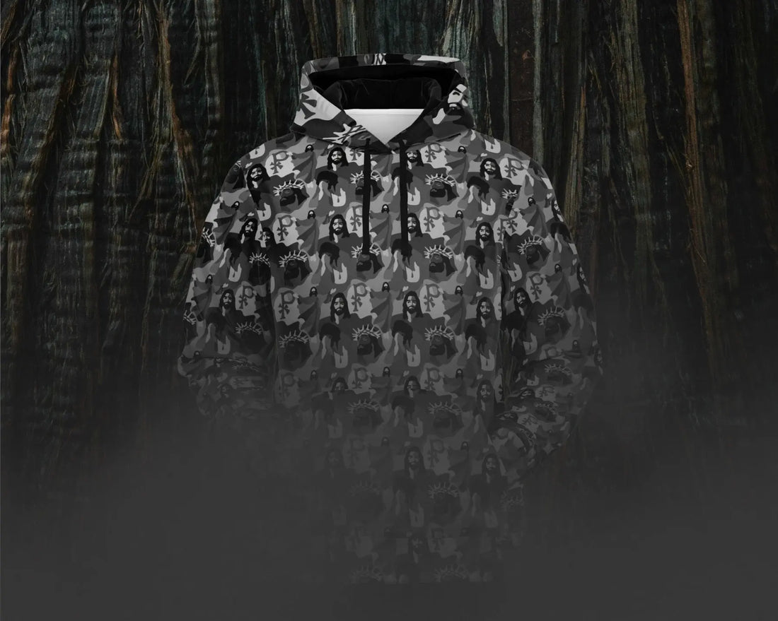 An image of a Jesus camo hoodie against a dark tree bark background with mist at the bottom portion of the image. Dark, moody, and evocative of the night of Jesus’ betrayal in the garden. 